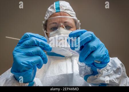 Una donna, tecnico di laboratorio, completamente coperta in una tuta protettiva bianca, fa un tampone di prova per controllare una possibile infezione con Coronavirus Foto Stock
