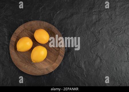 Piatto di legno di tre limoni freschi su superficie nera Foto Stock