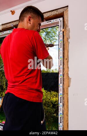 Dolyna, Ucraina 31 luglio 2020: Un dipendente installa un telaio per finestre, installando una finestra in plastica. Foto Stock