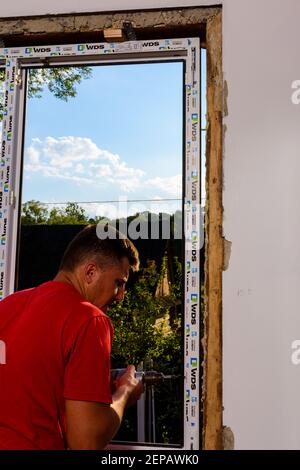 Dolyna, Ucraina 31 luglio 2020: Un dipendente installa un telaio per finestre, installando una finestra in plastica. Foto Stock