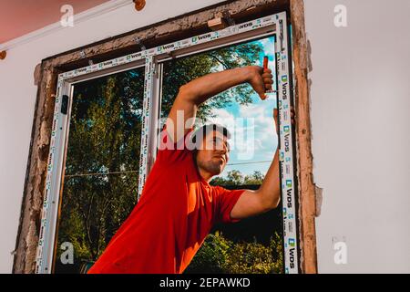 Dolyna, Ucraina 31 luglio 2020: Un dipendente installa un telaio per finestre, installando una finestra in plastica. Foto Stock