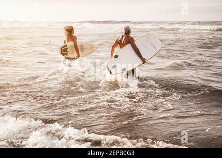 Padre e figlio che corrono sulla spiaggia al tramonto per Surf training - Focus sull'uomo giusto Foto Stock