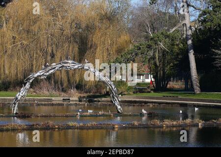 Hastings, East Sussex, Regno Unito. 27 Feb 2021. Regno Unito Meteo: La città balneare di Hastings crogiola nel caldo sole invernale con un sacco di persone che si allenano e camminano nel parco Alexandra che copre 108 ettari di parco ed è stato costruito nel 1878 dal rinomato giardiniere paesaggista Robert Marnock. Scultura del lago Continuum, serie di figure femminili interbloccanti che formano un arco nello stagno. La scultura è realizzata in piastre saldate in acciaio inox. Photo Credit: Paul Lawrenson/Alamy Live News Foto Stock