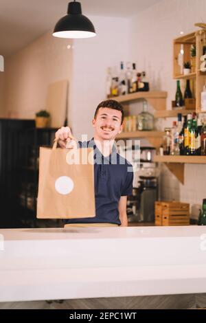 ritratto di un sorridente cameriere professionista che consegna un riciclato sacchetto di carta con ordine di prelievo Foto Stock