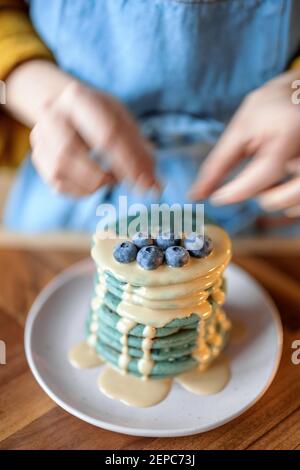 Donna decorare frittelle blu con mirtillo versato con caramello. Foto Stock