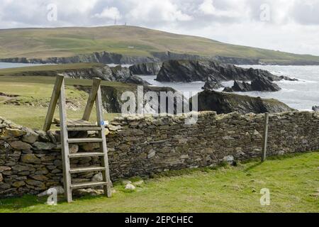 Una stiglia di legno a cavallo di un muro di pietra arenaria sull'isola di San Niniano, Shetland. Foto Stock