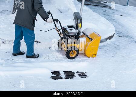 Uomo che pulisce il vialetto con macchine da neve dopo una tempesta di neve. Attrezzatura per la rimozione della neve in funzione sulla strada. Pulizia delle strade dalla neve. Nevica Foto Stock