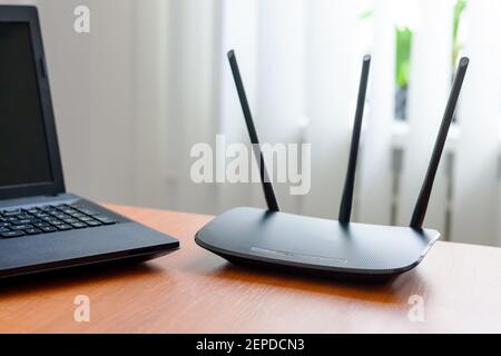 router wifi wireless e laptop su tavolo in legno all'interno. finestra dietro. concetto di connessione wireless. Foto Stock