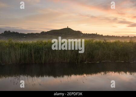 Dawn sopra Glastonbury Tor durante una mattinata nebbiosa sui livelli del Somerset. Foto Stock