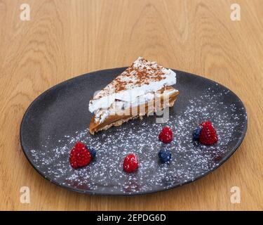 Fetta di caramello e torta di noci ricoperta da uno strato di crema, decorata con frutti di bosco e zucchero in polvere. Foto Stock