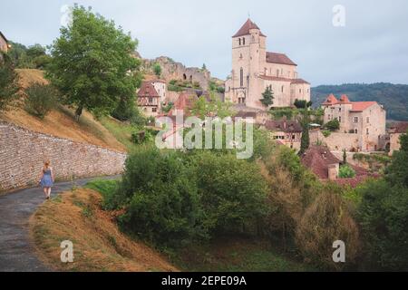 Una giovane turista caucasica in un abito estivo esplora il borgo medievale francese in cima alla collina di Saint-Cirq-Lapopie nella Valle del Lot, Francia. Foto Stock