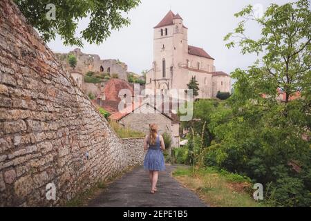 Una giovane turista caucasica in un abito estivo esplora il borgo medievale francese in cima alla collina di Saint-Cirq-Lapopie nella Valle del Lot, Francia. Foto Stock