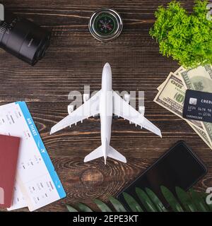 Miniatura di un aereo su un tavolo di legno con biglietti, documenti, denaro e altri accessori di viaggio. Concetto di vacanza e prenotazione. Vista dall'alto Foto Stock