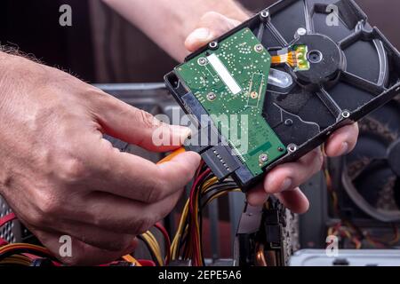 la persona tiene il disco rigido in polvere dal desktop per pulire o aggiornare il vecchio hardware rotto. primo piano dell'interfaccia di connessione dell'alimentazione e del disco rigido sata. Foto Stock