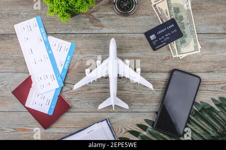 Miniatura di un aereo su un tavolo di legno con biglietti, documenti, denaro e altri accessori di viaggio. Concetto di vacanza e prenotazione. Vista dall'alto Foto Stock