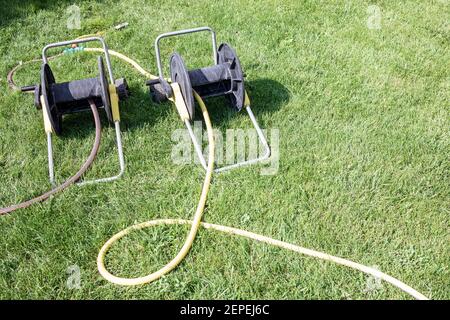 Due carrelli avvolgitubo a fondo erba verde del cortile estivo. Attrezzatura per giardinaggio. Copia spazio Foto Stock