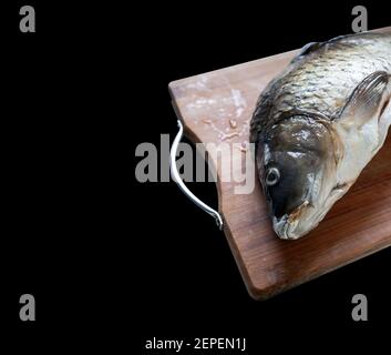 scongelamento del pesce carpa su tagliere di legno isolato su nero sfondo Foto Stock