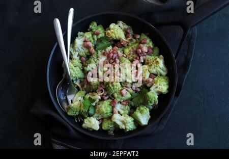 Broccoli romanesco fritto in padella con prosciutto e parmigiano isolato su fondo scuro. Vista dall'alto. Foto Stock