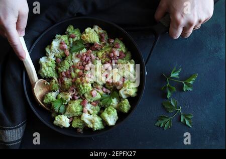 Broccoli romanesco fritto in padella con prosciutto e parmigiano isolato su fondo scuro. Vista dall'alto. Foto Stock