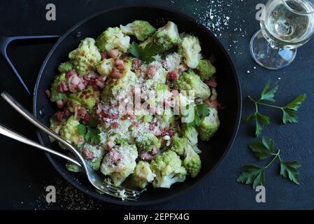 Broccoli romanesco fritto in padella con prosciutto e parmigiano isolato su fondo scuro. Vista dall'alto. Foto Stock