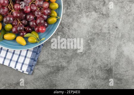Piatto blu di kumquat e uva rossa su marmo superficie Foto Stock