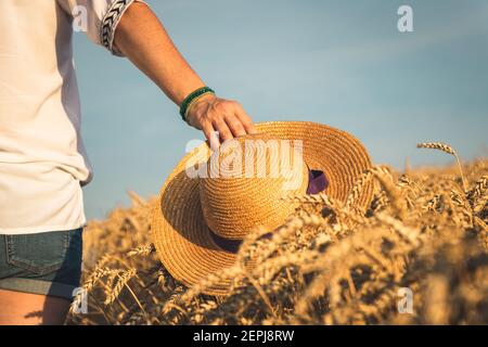 Donna con cappello di paglia che cammina nel campo. Gente spensierata all'aperto. Godimento dell'estate Foto Stock