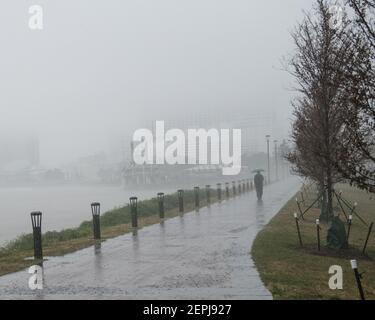 Figure sagomate con ombrelli camminano lungo il nebbioso lungofiume del Mississippi, passando davanti allo storico battello a vapore Natchez a New Orleans. Foto Stock