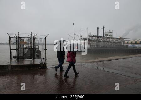 Figure sagomate con ombrelli camminano lungo il nebbioso lungofiume del Mississippi, passando davanti allo storico battello a vapore Natchez a New Orleans. Foto Stock