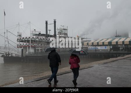 Figure sagomate con ombrelli camminano lungo il nebbioso lungofiume del Mississippi, passando davanti allo storico battello a vapore Natchez a New Orleans. Foto Stock