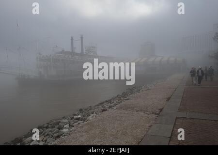 Figure sagomate con ombrelli camminano lungo il nebbioso lungofiume del Mississippi, passando davanti allo storico battello a vapore Natchez a New Orleans. Foto Stock