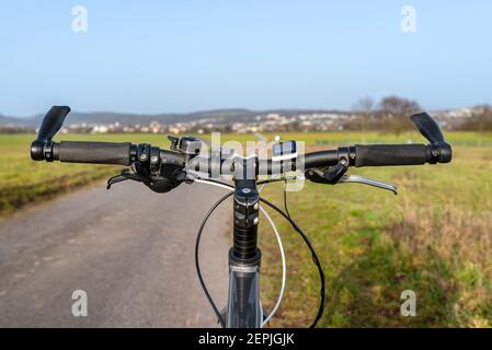 Manubrio per mountain bike visto dalla prospettiva della prima persona. Telaio per biciclette e accessori per biciclette visibili sul manubrio e la strada in ba Foto Stock