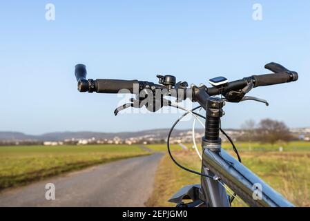 Manubrio per mountain bike visto dalla prospettiva della prima persona. Telaio per biciclette e accessori per biciclette visibili sul manubrio e la strada in ba Foto Stock