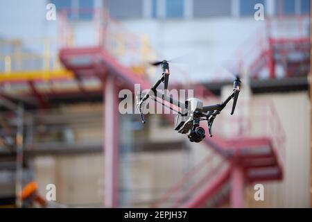 Quadricottero nero con potente fotocamera per una costruzione iindustriale sfocata. Ispezione visiva nell'industria. Foto Stock
