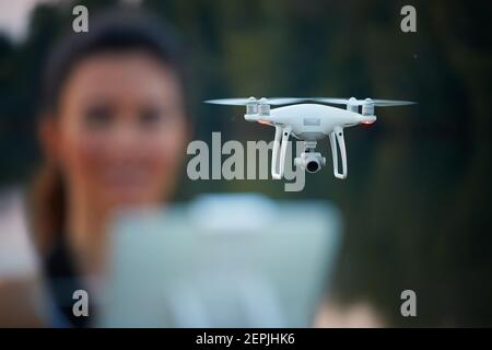 Giovane bella donna controlla un quadricottero bianco da telecomando con un tablet. Focalizzato sul drone, il pilota è fuori fuoco. Insegnare volare Foto Stock