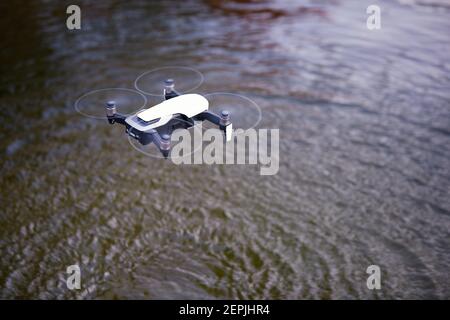 Vista dall'alto su un piccolo quadricottero intelligente che si trova in aria su una superficie d'acqua. Cerchi sull'acqua causati dal flusso d'aria. Test dei sensori dei droni. Foto Stock