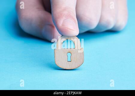 persona privacy e sicurezza concetto. persona caucasica tiene in legno lucchetto su sfondo blu. copia spazio Foto Stock