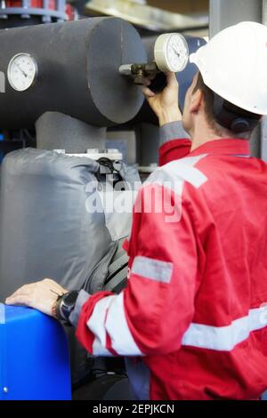 Industria dell'energia. Un tecnico vestito con tute rosse e un casco bianco che controlla i parametri di riscaldamento. Tecnologia di distribuzione dell'acqua di riscaldamento. Foto Stock
