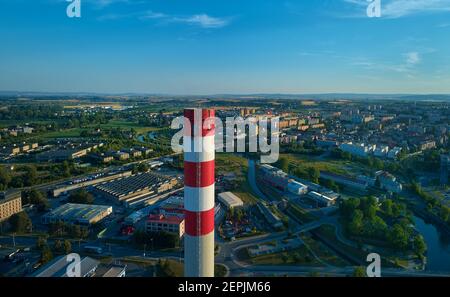 Vista aerea di alto camino della centrale termica, dipinta di bianco e rosso contro la città popolata sullo sfondo. Foto Stock