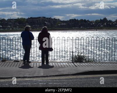 Due donne in piedi accanto recinzione guardando verso la soleggiata West Bay, North Berwick Foto Stock