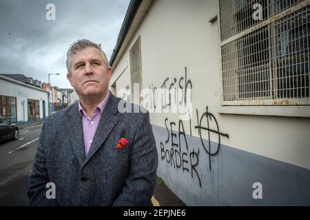 LARNE, IRLANDA DEL NORD - Febbraio, 24 : Keith Turner UUP in piedi di fronte a minacciosi graffiti lealisti puntati al personale portuale a Larne, Nord Foto Stock