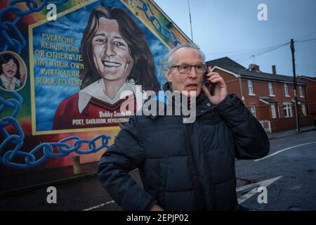 BELFAST, IRLANDA DEL NORD - Febbraio, 23 Gerry Kelly di fronte al murale di Bobby Sands presso la sede centrale del Sinn Fein riceve una chiamata per l'allerta contro la bomba Foto Stock