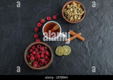 Tazza di tè con lamponi freschi e camomilla su nero sfondo Foto Stock