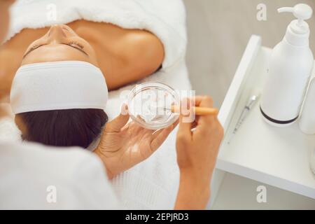 Mani di estetista mescolando maschera idratante con spazzola da applicare sulla pelle del viso delle donne durante la cura della pelle Foto Stock