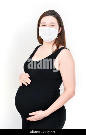 Donna incinta che indossa una maschera facciale bianca. Protezione preventiva del coronavirus. Concetto di una gravidanza sana durante una pandemia. Foto Stock