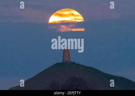 Glastonbury, Somerset, Regno Unito. 27 febbraio 2021. Regno Unito Meteo. La luna piena di neve si innalza da dietro uno strato di nube a Glastonbury Tor nel Somerset al crepuscolo. Picture Credit: Graham Hunt/Alamy Live News Foto Stock