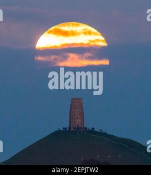 Glastonbury, Somerset, Regno Unito. 27 febbraio 2021. Regno Unito Meteo. La luna piena di neve si innalza da dietro uno strato di nube a Glastonbury Tor nel Somerset al crepuscolo. Picture Credit: Graham Hunt/Alamy Live News Foto Stock