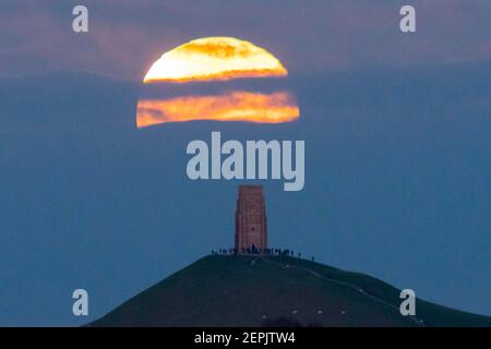 Glastonbury, Somerset, Regno Unito. 27 febbraio 2021. Regno Unito Meteo. La luna piena di neve si innalza da dietro uno strato di nube a Glastonbury Tor nel Somerset al crepuscolo. Picture Credit: Graham Hunt/Alamy Live News Foto Stock