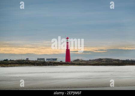 Vista sul faro rosso dell'isola olandese Schiermonnikoog su una spiaggia, tempesta che soffia sabbia sulla spiaggia Foto Stock