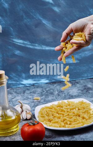 La donna versa i fusilli crudi nel piatto con pomodoro e aglio Foto Stock