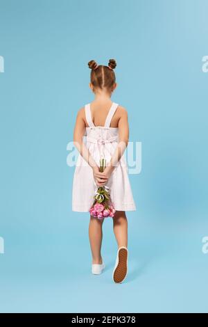 bambina con bouquet di rose dietro la schiena su sfondo blu studio. vista posteriore Foto Stock